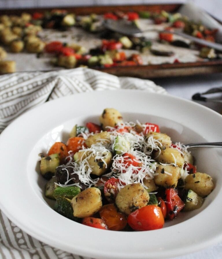 a picture of sheet pan gnocchi plated in a white bowl with a fork and a sheet pan in the background
