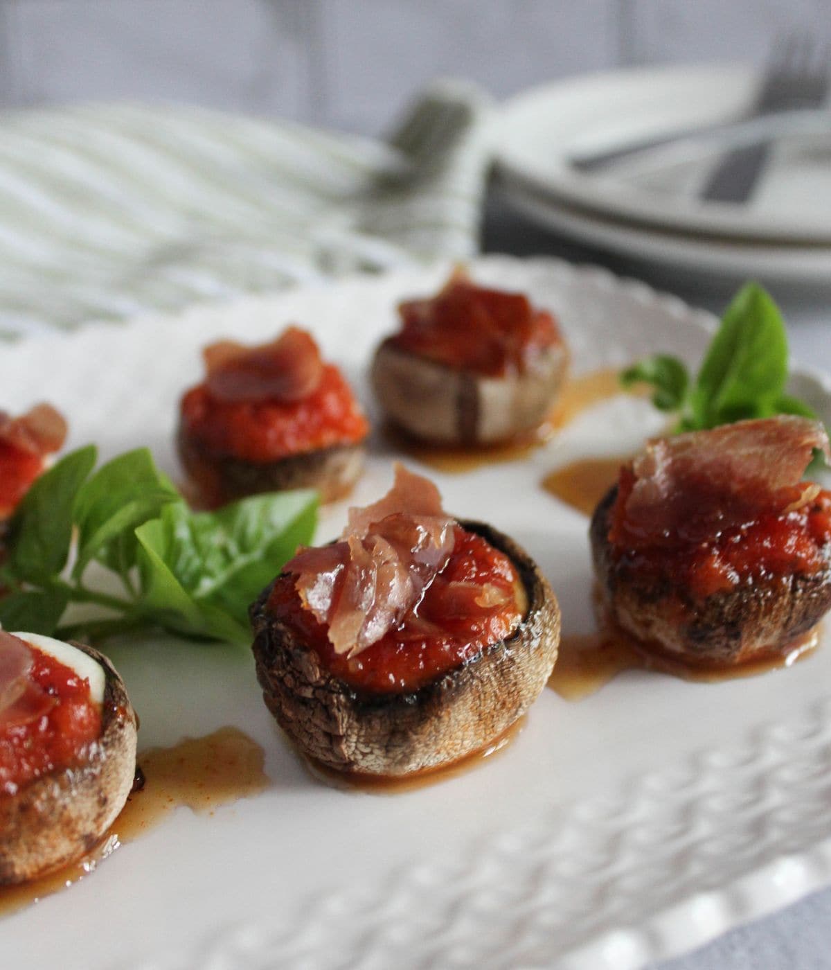 Delicious pizza stuffed mushrooms garnished with basil on a white plate.